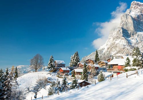 Travel to Switzerland in the winter. Alpine Village in the snow. Traditional houses with red shutters and roofs.